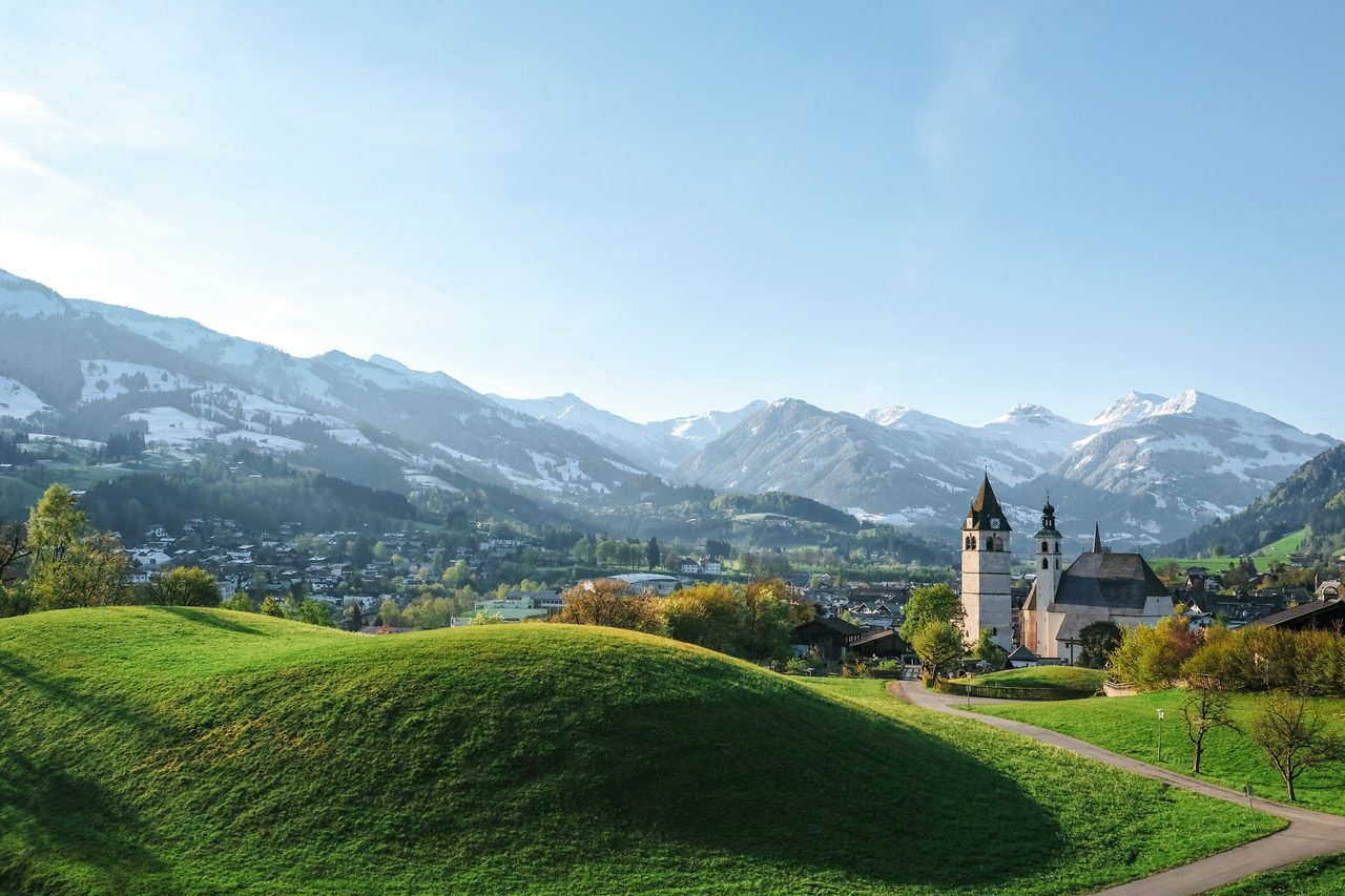 Kitzbühel mit Kirche und grünen Wiesen vor den Alpen
