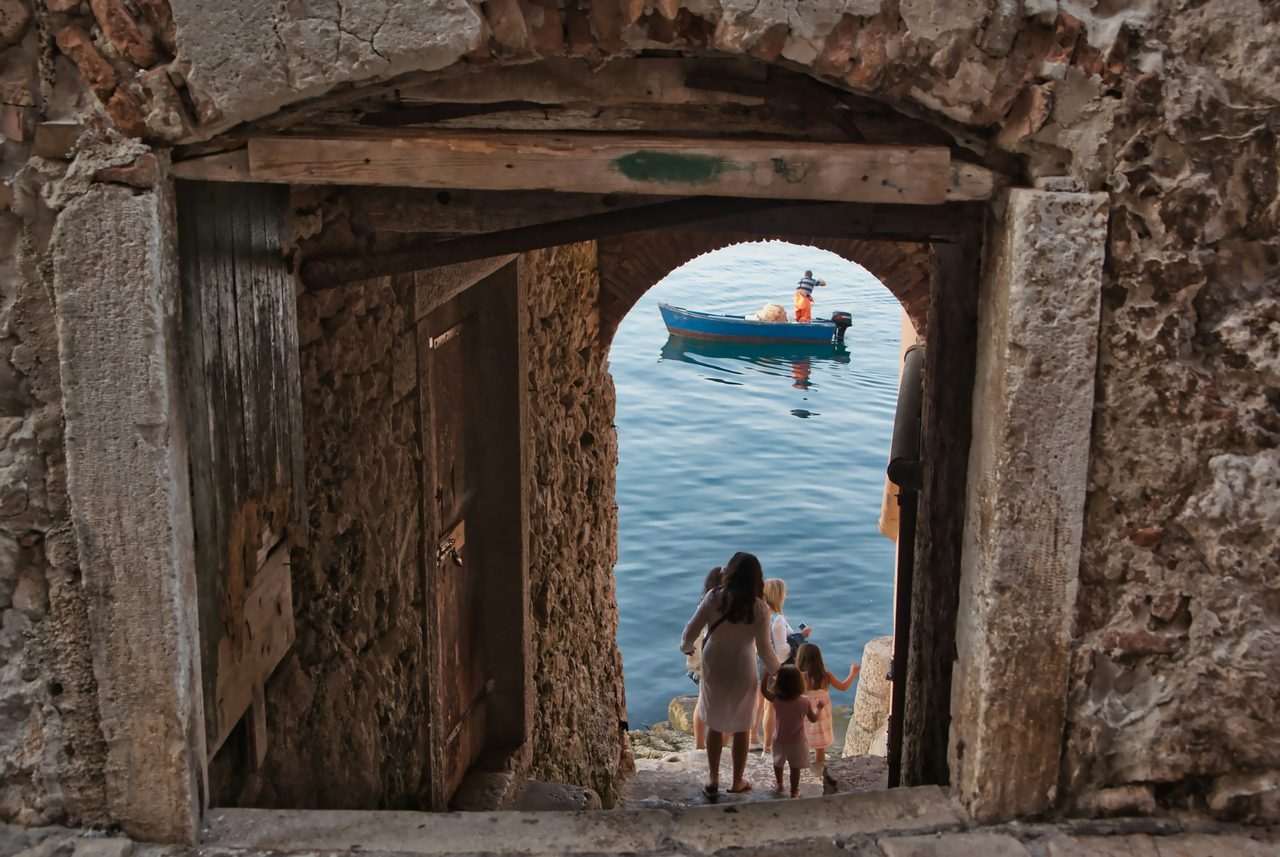 Mutter und Kind gehen in Rovinj durch ein steinernes Tor zum Meer