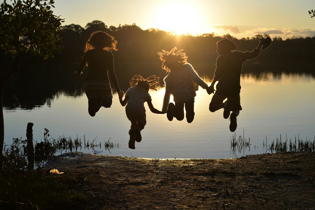 Kinder springen bei Sonnenuntergang Hand in Hand ins Wasser