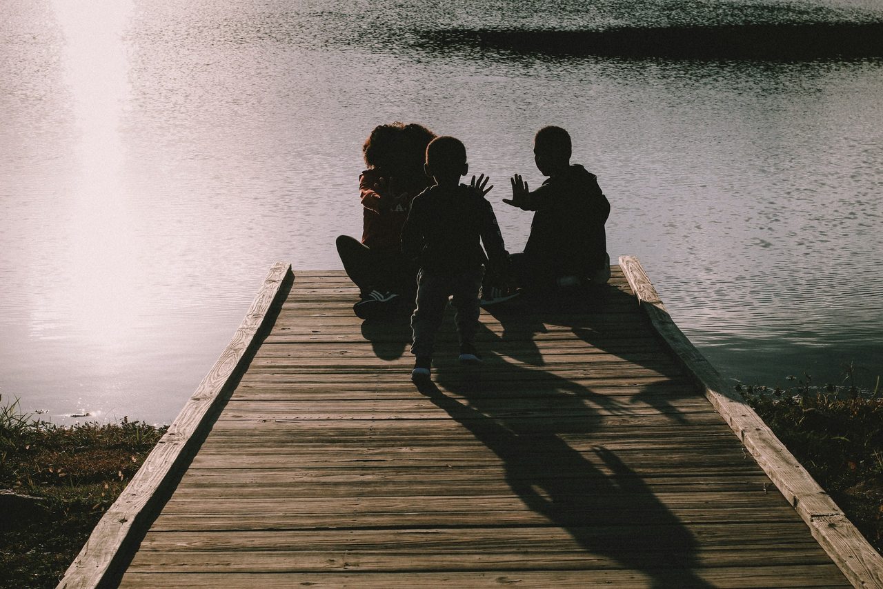 Familie sitzt im Abendlicht auf einem Holzsteg am See